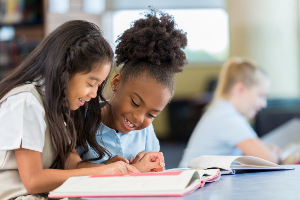 Two girls are reading a book together.