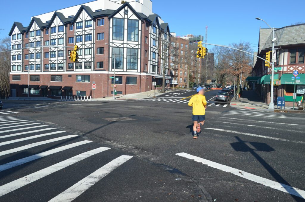 A person in yellow jacket crossing street at intersection.